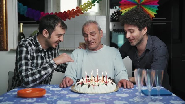 happy Old father blows the candles of his birthday cake surrounded by his sons