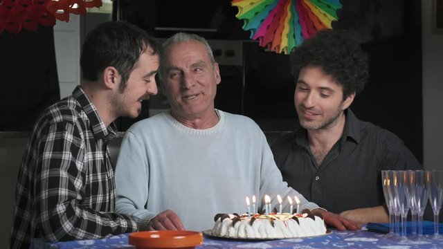 smiling Old father blowing on the candles on his birthday cake with his sons