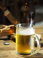 Beer in a glass and a bottle on a wooden table for work, with a knife and a log on the side.