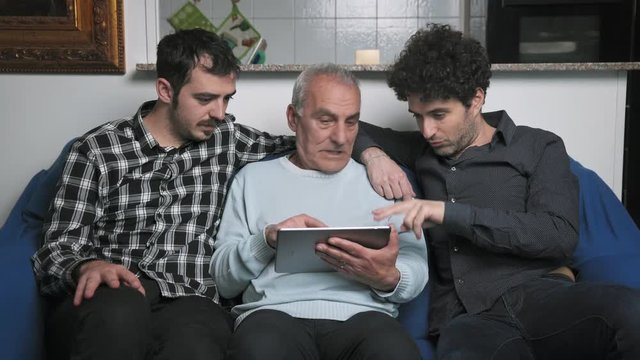 Old Father is helped by patient sons to learn using digital tablet-indoor