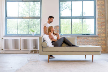 Obraz premium A beautiful young woman lying on the sofa with boyfriend hugging her from behind.