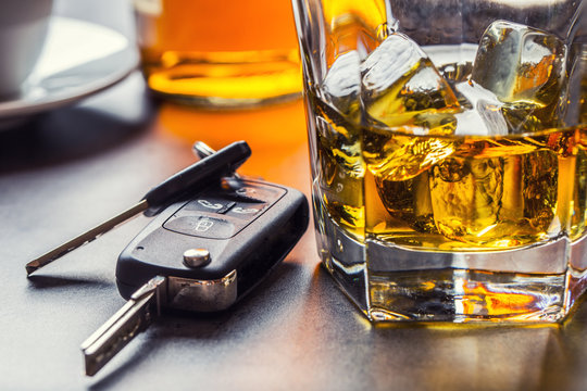 Car keys and glass of alcohol on table.