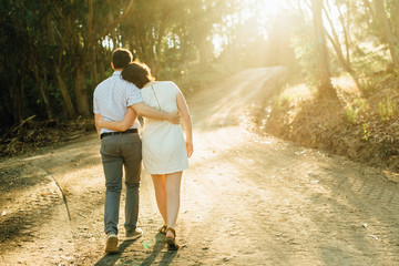 Young couple in love walking in the sunlight in the forest, holding hands, photographed from behind