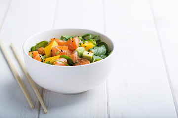 Hawaiian Poke salad with salmon, avocado and vegetables in a bowl on a white wooden rustic background with copy space, vegetables and chopsticks. Horizontal