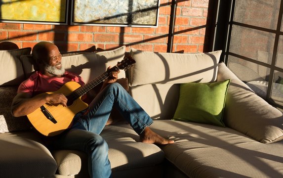 Smiling senior man playing guitar while sitting on sofa at home