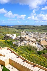 Fototapeta na wymiar Elevated view of fortified buildings and the landscaped old moat within the citadel with views over the town rooftops towards the countryside and sea, Victoria (Rabat), Gozo, Malta.