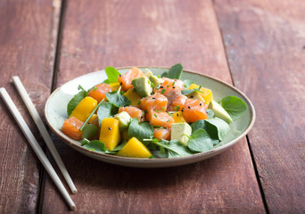 Hawaiian Poke salad with salmon, avocado and vegetables on the plate on a rustic background