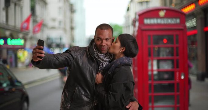 Black male and female taking selfies together while in London, England, Traveling African boyfriend and girlfriend taking photos near red phone booth in London street, 4k