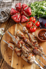 Shish kebab from pork on a wooden background. Appetizing meat cooked on an open fire and fresh vegetables. Rustic.