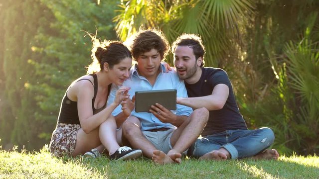 Young Friends sitting on a meadow using Digital Tablet - slow motion