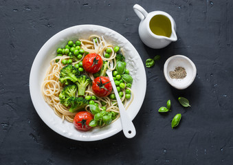 Fototapeta na wymiar Veggie pasta. Vegetarian lunch - spaghetti with broccoli cabbage, green peas and cherry tomatoes on dark background, top view. Healthy food concept
