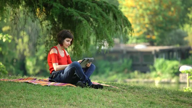 Beautiful woman relaxes sitting on the lawn using the tablet