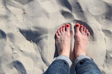 woman's feet with pedicure red nails on sand