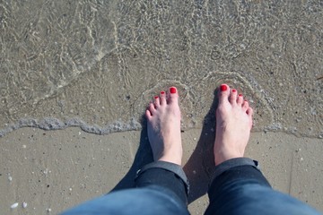 woman's feet with pedicure red nails on sand