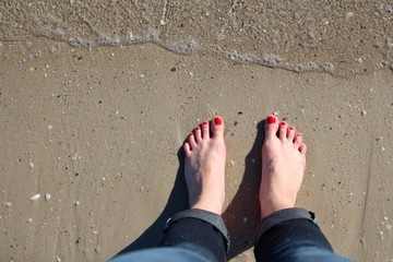 woman's feet with pedicure red nails on sand