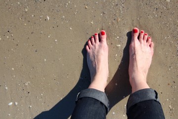 woman's feet with pedicure red nails on sand