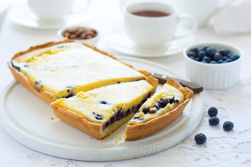 Tea time. Homemade blueberry cheesecake, cups of tea, nuts and berry on white table cloth