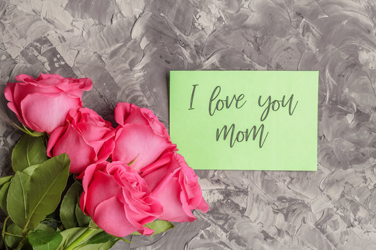 Pink roses and a green card with the inscription I love you mom on a gray concrete background