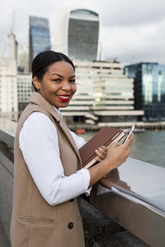 UK, London, portrait of smiling businesswoman standing on bridge with cell phone