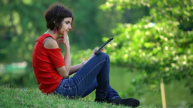 Happy and relaxed Woman sitting on the fgrass With Tablet  In Park