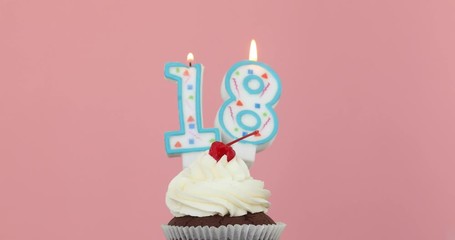 Number eighteen 18 candle in a cupcake against a pastel pink background blow out at the end - Powered by Adobe
