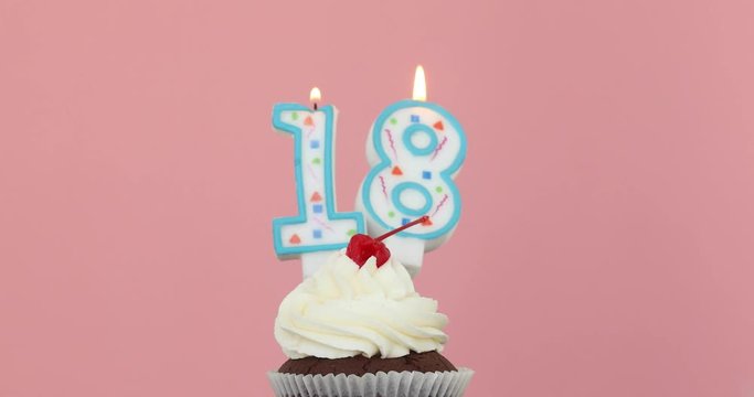 Number eighteen 18 candle in a cupcake against a pastel pink background blow out at the end