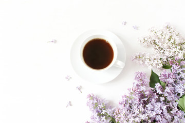 Obraz na płótnie Canvas Floral composition made of beautiful purple lilac, syringa flowers on white wooden background with cup of coffee. Feminine office desk, styled stock image, flat lay, top view with empty space.