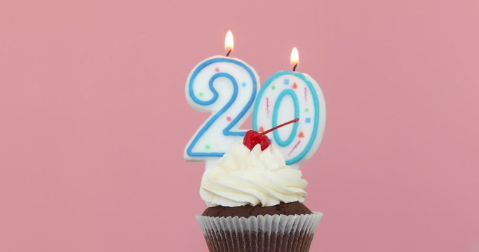 Number Twenty 20 candle in a cupcake against a pastel pink background blow out at the end