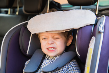 Portrait of the cute little boy who is sitting in the baby car seat in a car and compressing his teeth