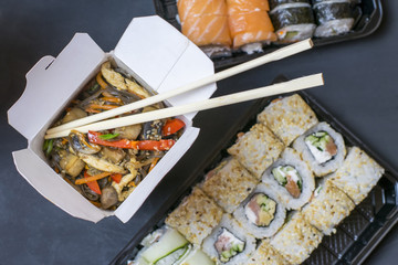 Delivery of a hot lunch in a box. Lapshi with chopsticks on the background of rolls.