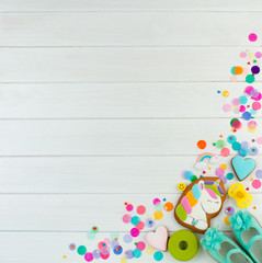 Baby shoes and unicorn cookie on white wooden party background with copy space