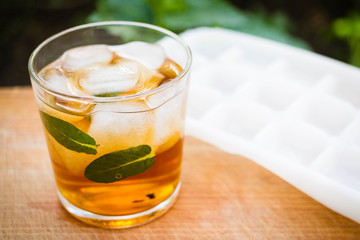 cold tea with ice and mint in a glass on a wooden background in the garden