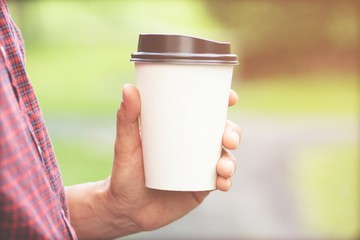 people business man hand holding paper cup of take away drinking coffee on natural morning sunlight. space Place for your text or logo.