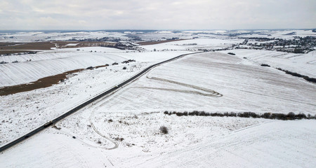 Fototapeta na wymiar View from the air on the winter road in the field on which cars are going