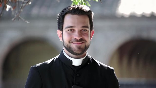 Portrait Of young Catholic Priest smiling at camera outdoor