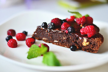 Delicious brownie lies on a plate decorated with mint leaves, blueberry and raspberry