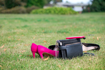 Ladies purse, pink high heel shoes and smart phone left in the grass. Girls freedom concept