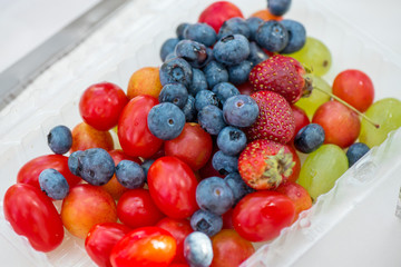Strawberries, grapes, blueberries and tomatoes in plastic bowl. Healthy eating concept 