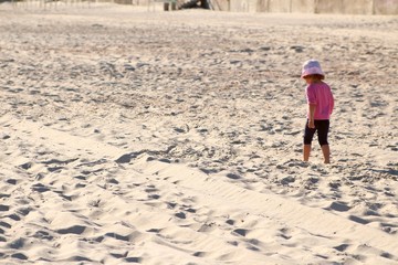 little girl in pink shirt and panama and blue shirts goes along the beach