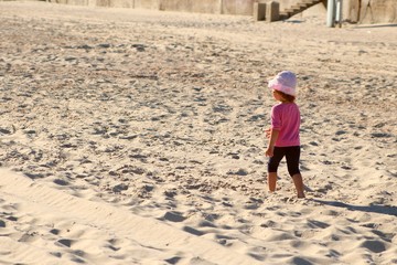 little girl in pink shirt and panama and blue shirts goes along the beach