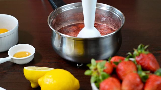 Closeup of grinding fruit with immersion blender in a stainless steel saucepan, cooking sauce, jam, confiture of strawberry.