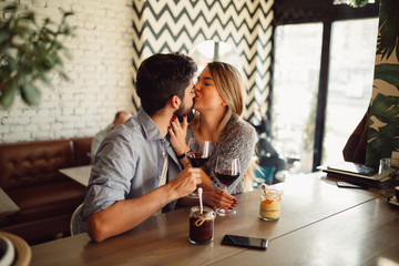 While they drinking wine at cafe young blonde woman is kissing her boyfriend