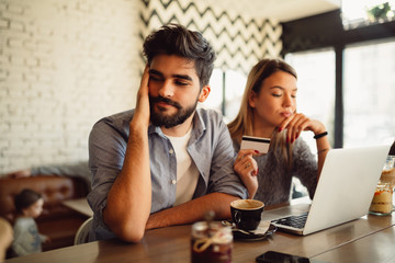 Young couple with notebook and credit card drinking coffee in cafe