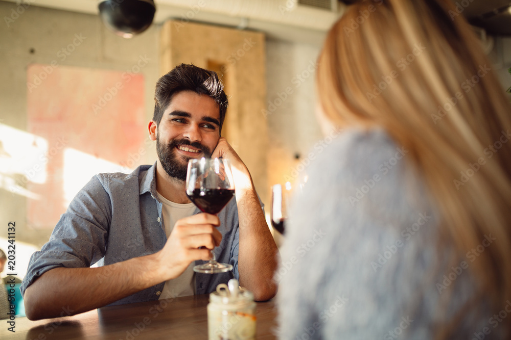 Wall mural young handsome man is drinking wine with his girlfriend at cafe