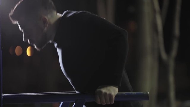 Sportsman pushups on horizontal bars at night, workout anywhere