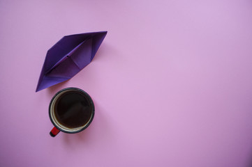 A cup of coffee and paper ship on violet background.