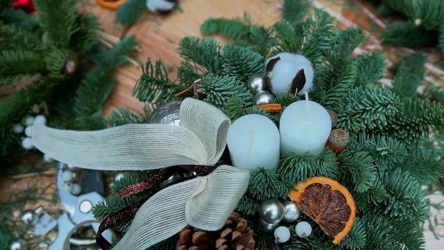 Christmas composition: pine tree branches, candles, christmas tree toys, bow, dry orange slices and cotton flower balls in a basket. Craft supply for handcrafted decorations on wooden table, close-up