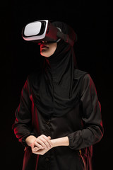 Portrait of beautiful smart young muslim woman wearing black hijab using virtual reality headset on black background