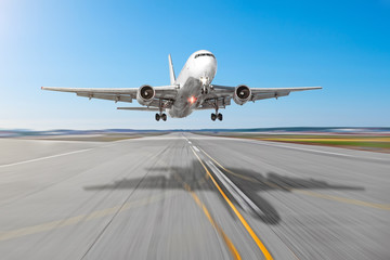 Fototapeta na wymiar Passenger aircraft with a cast shadow on the asphalt landing on a runway airport, motion blur.