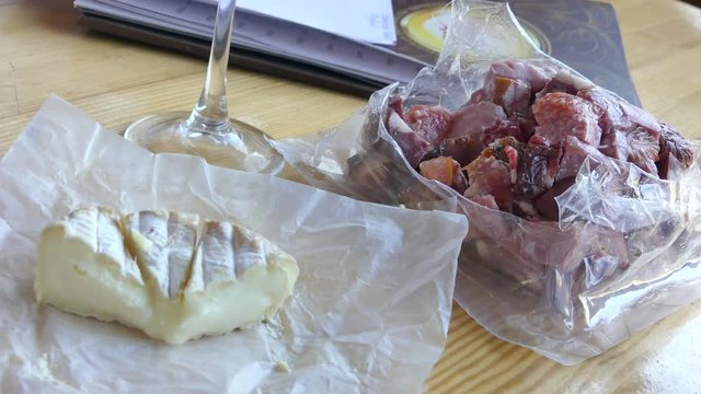 The head of the French cheese on the table on the background of women's hands, cuts the packaging with smoked meat and sausage.